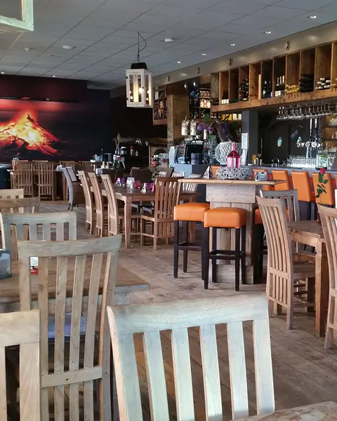Het restaurant van Paviljoen Stormvogel: houten tafels, oranje barkrukken en de lange bar met wijnrekken