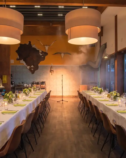De feestzaal met houten balken, 's avonds gedekt met lange tafels, witte kleden en kaarsen (AI-beeld)