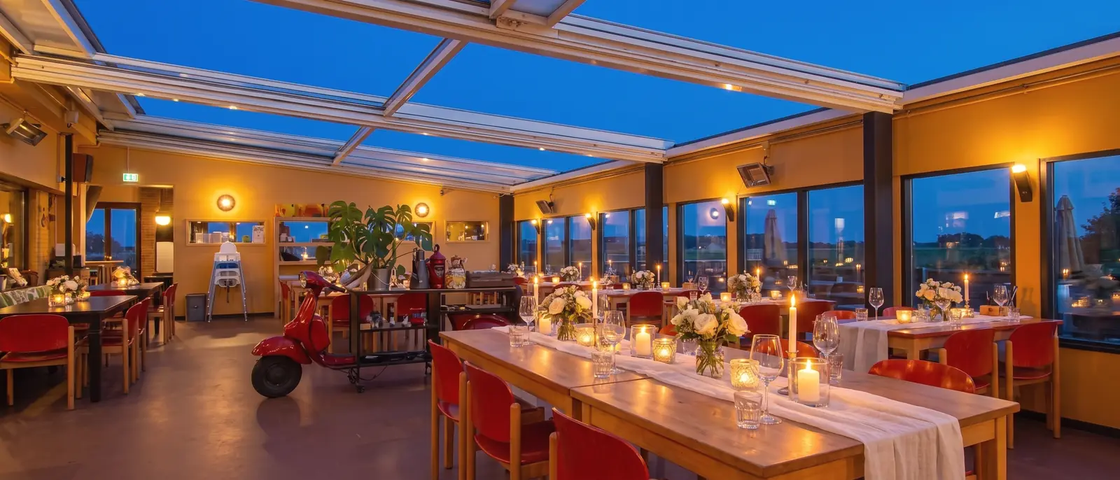 De serre met schuifdak bij blauw uur, de tafels tot één lange feesttafel gedekt met kaarsen en bloemen (AI-beeld)