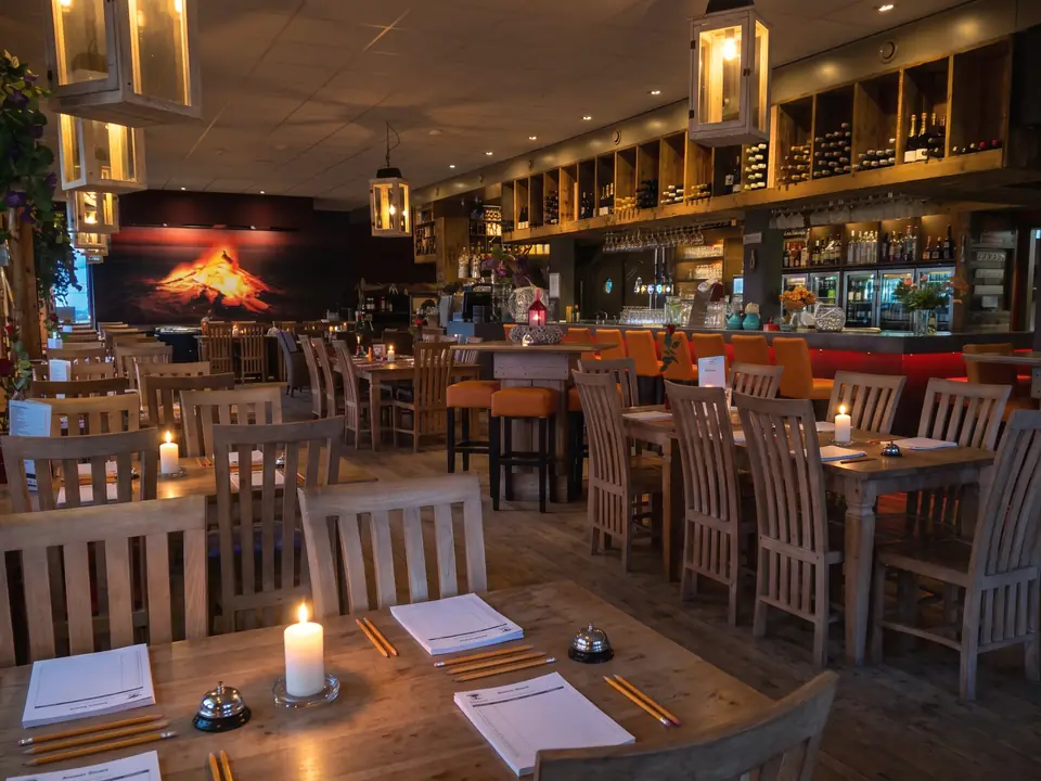 Het restaurant 's avonds met kaarsen, op de tafels lege antwoordformulieren, potloden en een belletje (AI-beeld)