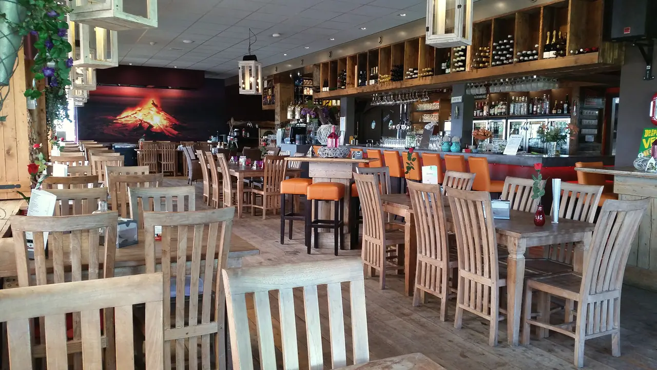 Het restaurant overdag: houten tafels en stoelen, oranje barkrukken, de vulkaanwand en de bar met wijnrekken